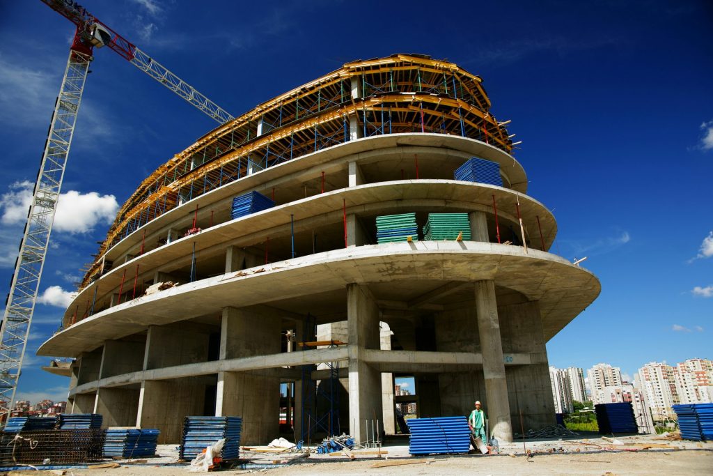 Vista en contrapicado de un edificio circular en construcción con una grúa, cielo azul despejado.