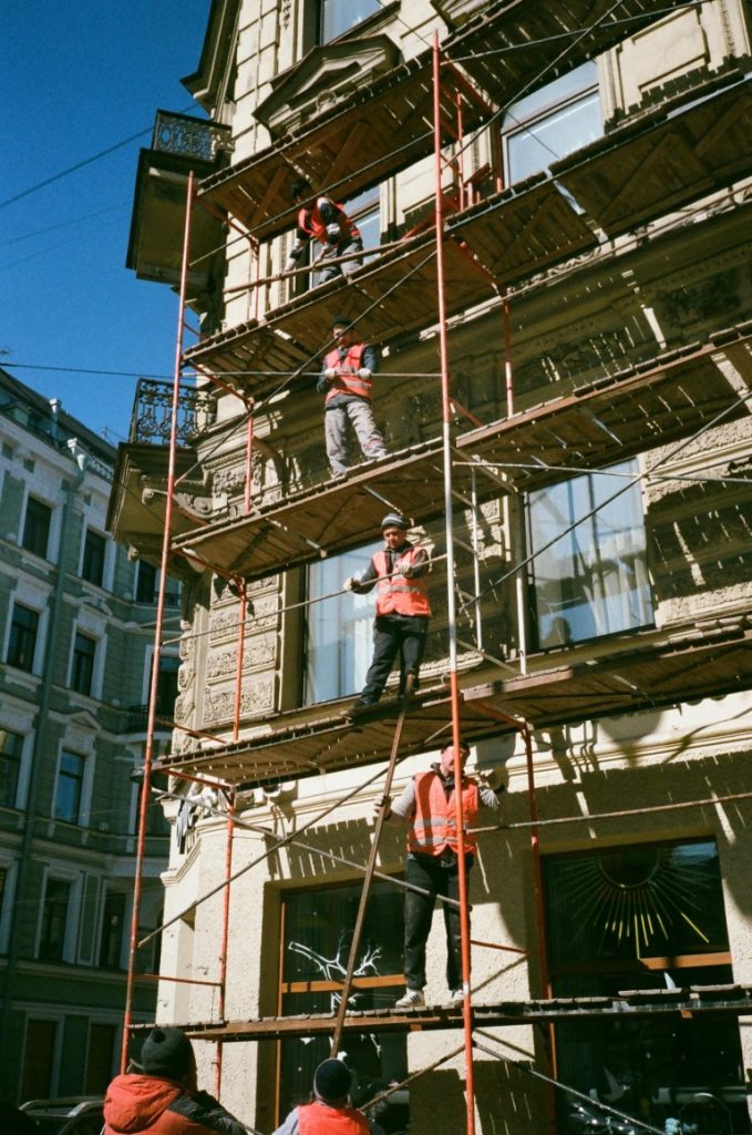 Obreros de la construcción sobre andamios renovando la fachada de un edificio en un día soleado.