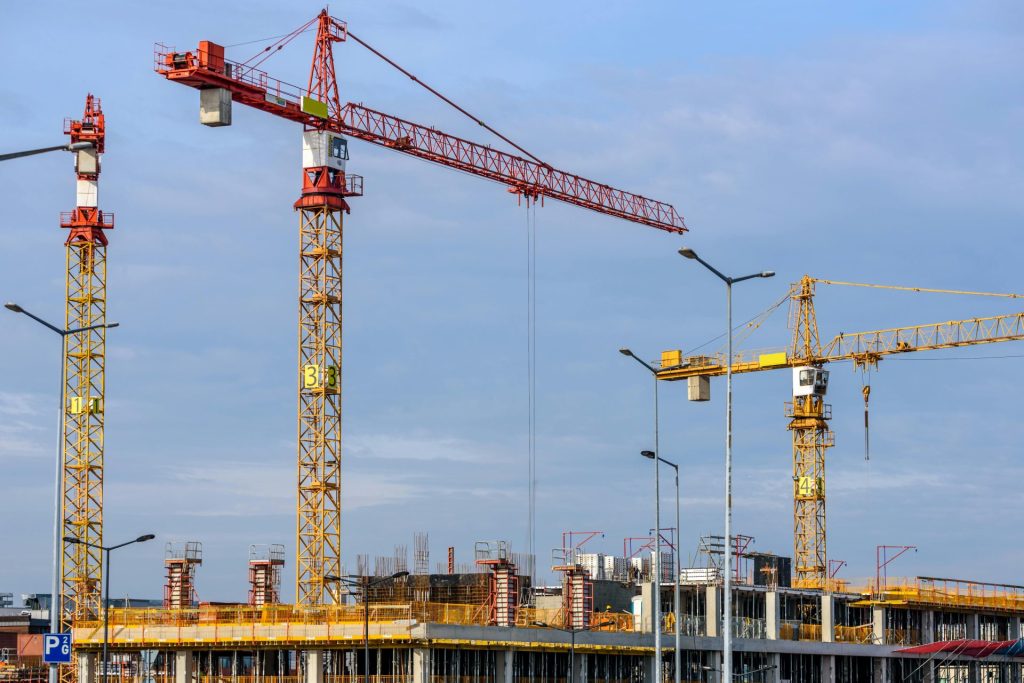Varias grúas torre trabajando en una gran obra en construcción con un cielo azul de fondo.